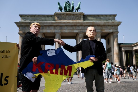 epa12299726 Activists wearing masks of US President Donald J. Trump (L) and Russian President Vladimir Putin (R) hold a sign in the shape of the Crimean Peninsula in the colors of the Ukrainian flag d ...
