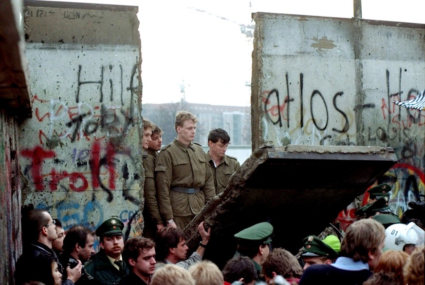 ARCHIVE --- VORSCHAU 30. JAHRESTAG MAUERFALL BERLIN AM 9. NOVEMBER 2019 --- DDR-Grenzsoldaten schauen am 11. November 1989 durch ein Loch, das Jugendliche in die Berliner Mauer gestemmt haben. Der Unt ...
