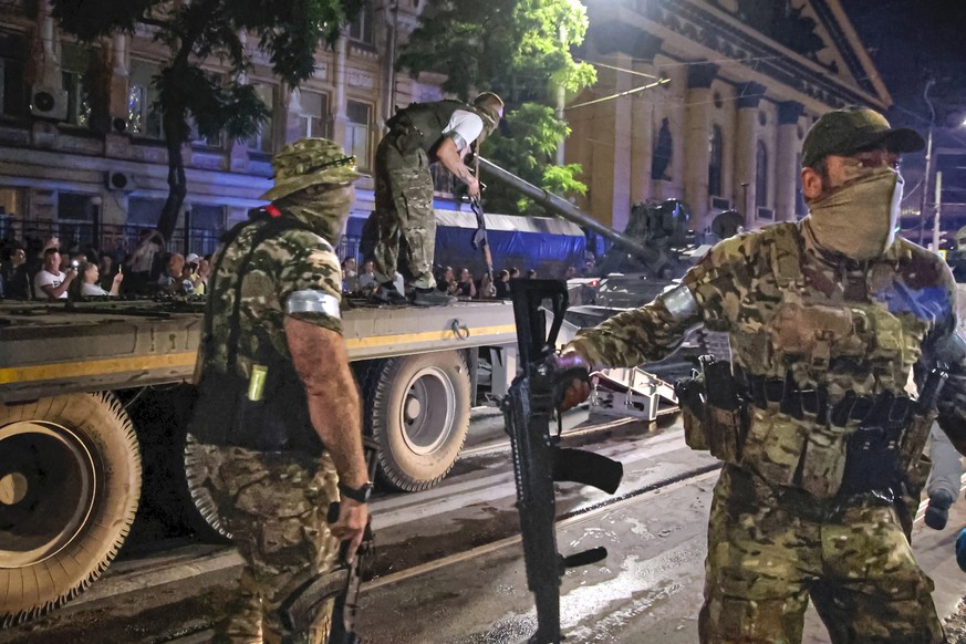 FILE - Members of the Wagner Group military company guard an area as other load their tank onto a truck on a street in Rostov-on-Don, Russia, Saturday, June 24, 2023, prior to leaving an area at the h ...