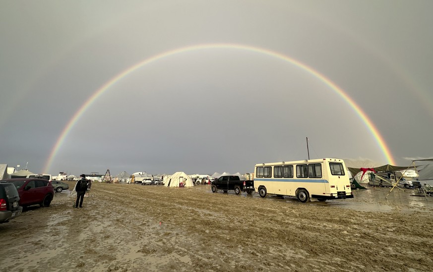epa10838248 A person walks in the mud under a rainbow at the Burning Man Festival in the Black Rock Desert, Nevada, USA, 02 September 2023 (issued 03 September 2023). Heavy rains in the normal dry loc ...