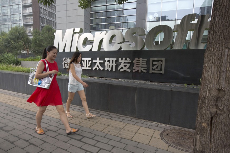 In this photo taken Thursday, July 31, 2014, women walk past the logo for Microsoft in Beijing, China. Chinese regulators have launched a series of anti-monopoly investigations of global automakers an ...