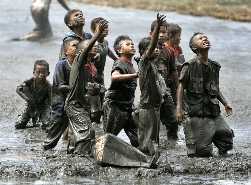 FILE - Dalam file foto bertanggal 17 Januari 2005 ini, anak-anak pengungsi mencoba menangkap barang-barang bantuan yang dijatuhkan dari helikopter militer Australia ke sawah di Lambaya, di pinggiran Banda Aceh, Indonesia...
