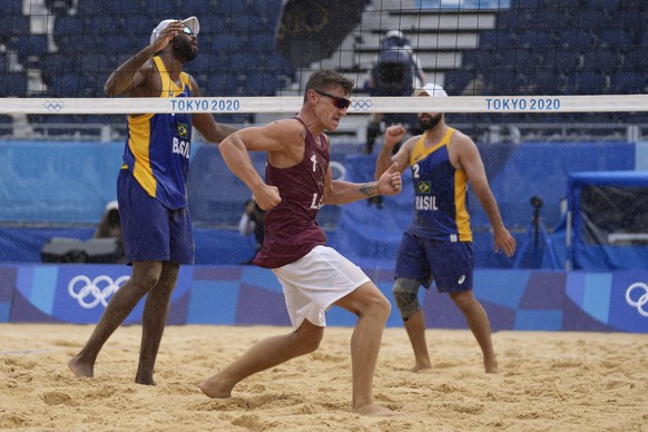 Martins Plavins, center, of Latvia, celebrates winning men&#039;s beach volleyball match against Evandro Goncalves Oliveira Jr., left, of Brazil, and teammate Bruno Oscar Schmidt at the 2020 Summer Ol ...