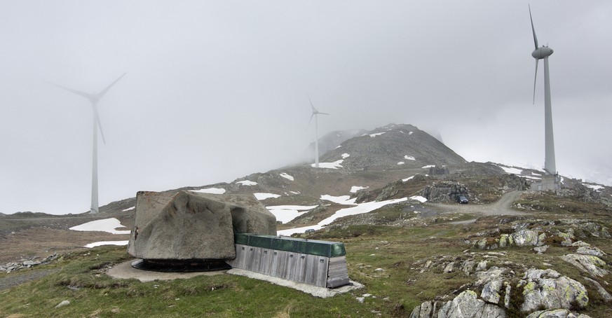 Three of the four wind turbines of the Elektrizitaetswerk Ursern power plant stand in the background, and in the foreground, there is an old Swiss military cannon camouflaged as a stone, pictured on M ...