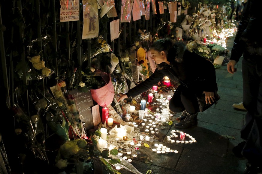 People kneel as they light candles to pay tribute to victims near the site of the attack at the Bataclan concert hall in Paris, France, November 18, 2015. REUTERS/Gonzalo Fuentes