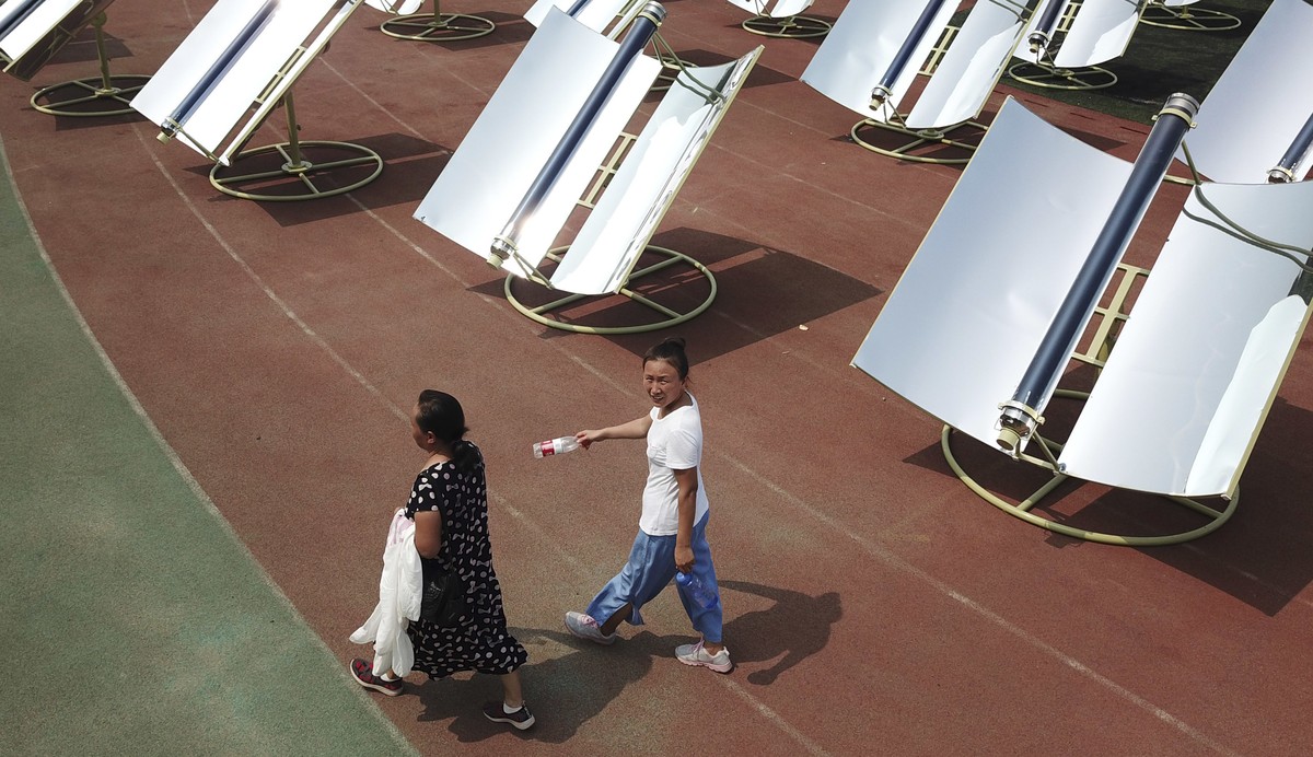 In this photo taken Thursday, Aug. 2, 2018, women walk past rows of solar cookers which use reflective mirrors to heat metal and glass vacuum tubes up to 400°C (275°F) to cook food during a solar food ...