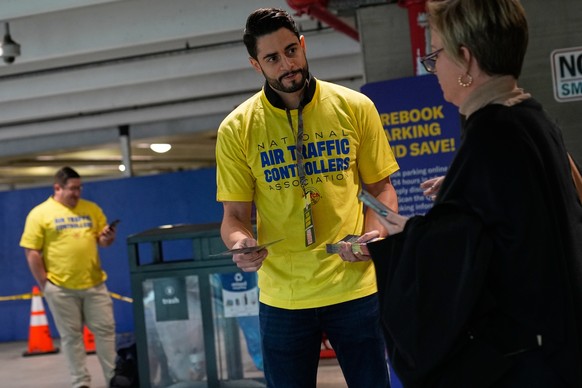Jose Rodriguez, an air traffic controller, hands out pamphlets urging travelers to contact their representatives to help stop the government shutdown at LaGuardia Airport in New York, Tuesday, Oct. 28 ...