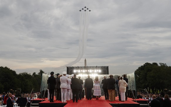 President Donald Trump and first lady Melania Trump gather with others on stage as the Blue Angels, the United States Navy&#039;s flight demonstration squadron, flies overhead during an Independence D ...