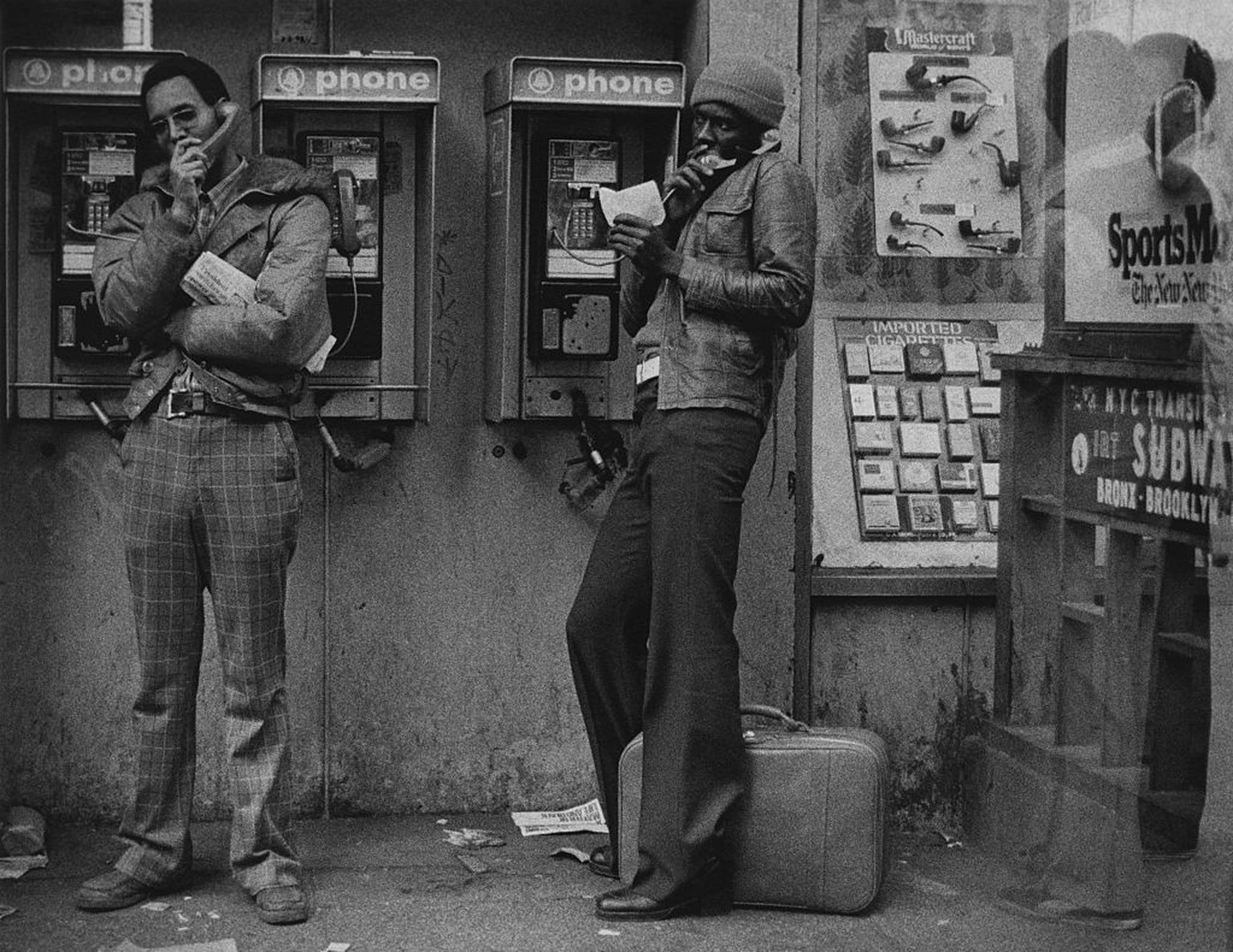 Two young men make phonecalls on a payphone by a subway station near Times Square, New York City, circa 1975. (Photo by Erika Stone/Getty Images)