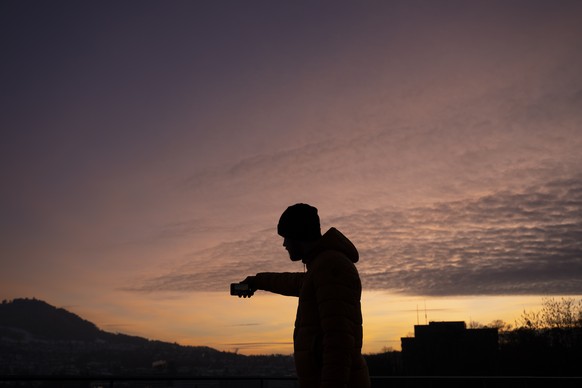 A man takes a picture with his smartphone during a cold sunset from the Federal terrace (Bundesplatz), in Bern, Switzerland, Sunday, December 18, 2022. (KEYSTONE/Anthony Anex)