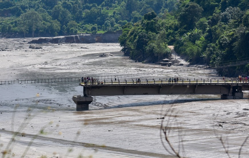 Hundreds missing after deadly flooding near Nepal-Tibet border - Nuwakot People stand on the remains of a bridge swept away by floodwaters in Nuwakot, Nepal, on August 26, 2026, following a powerful f ...