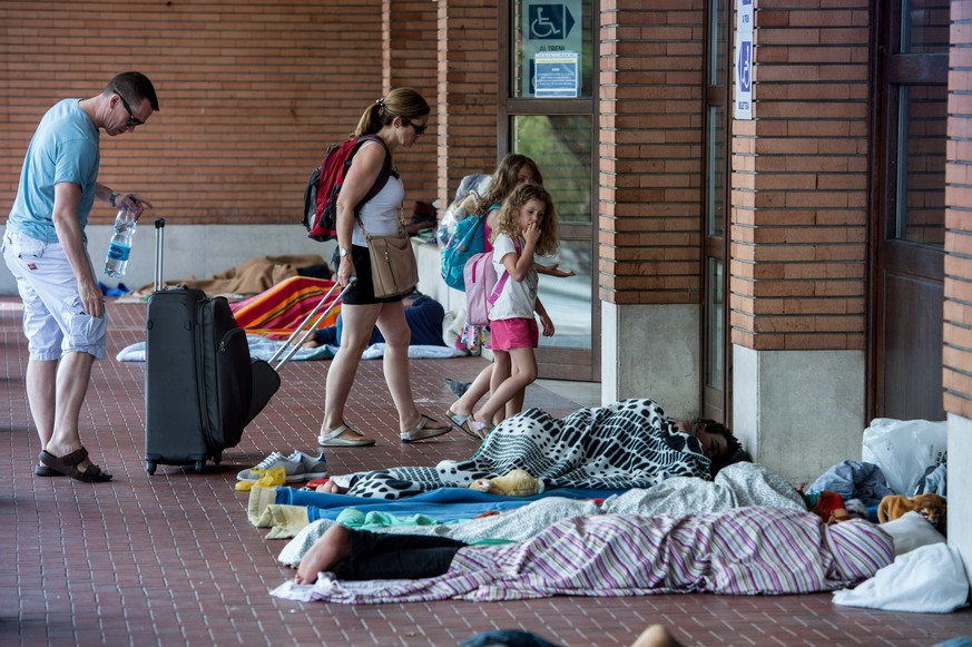 Touristen passieren am Boden schlafende Fluechtlinge, welche sich am Bahnhof von Como niedergelassen haben und auf eine Weiterreise in die Schweiz warten, am Dienstag, 2. August 2016, in Como, Italien ...