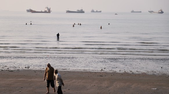 KEYPIX - Men walk on the shoreline as people wade in the water in the Strait of Hormuz, where cargo and service vessels are anchored off Bandar Abbas, Iran, Monday, June 1, 2026. (Amirhosein Khorgooi/ ...
