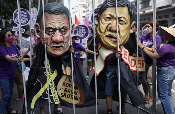 Protesters wearing masks portraying Philippine President Rodrigo Duterte, left, and former senator Ferdinand &quot;Bongbong&quot; Marcos Jr., the son of the late dictator Ferdinand Marcos, stands behi ...