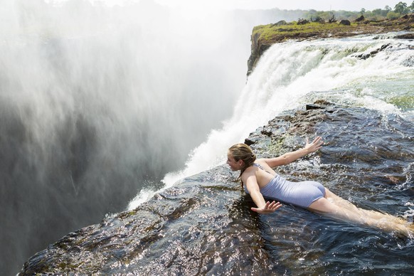 Young girl in the water at the Devils Pool lying on her front, arms spread out, at the edge of the cliff of Victoria Falls. Victoria Falls,Zambia,Young girl in the water at the Devils Pool lying on he ...
