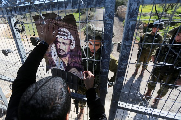 Ein Aktivist aus Palästina hängt ein Plakat von Jassir Arafat auf.