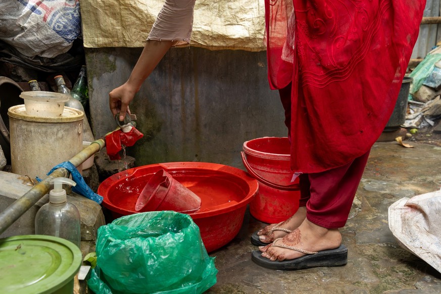 Eine Frau zapft Wasser an. Bastuhara Slum Bangladesch.