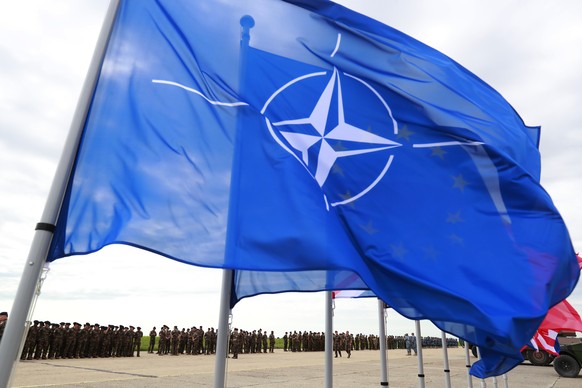 epa10014202 The NATO flag waves in the wind as troops stand in line before being reviewed by French President Macron at Mihail Kogalniceanu Air Base, near the city of Constanta, Romania, 15 June 2022. ...