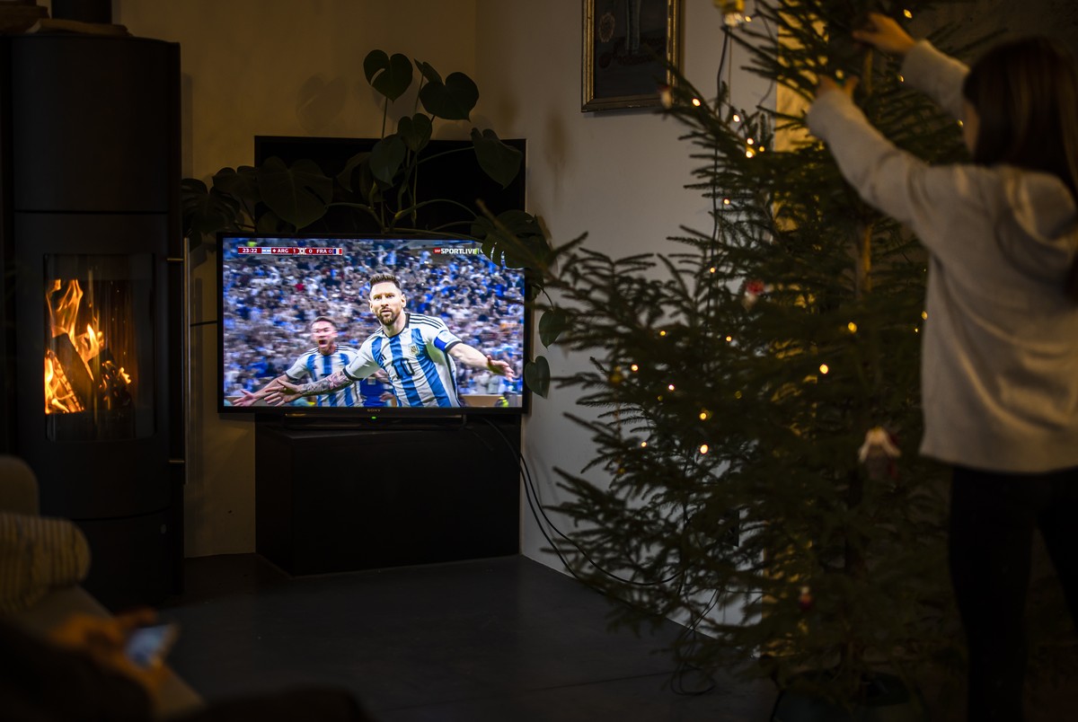A girl decorates a Christmas tree next to a television showing Argentina's Lionel Messi celebrating a goal during the FIFA World Cup Qatar 2022 Final match, in Zurich, Switzerland, on Sunday, Dec ...