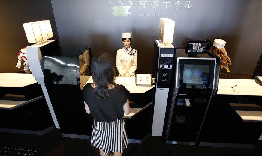 A receptionist robot, top center, accompanied by two other robots, greets a hotel employee demonstrating how to check in the new hotel, aptly called Henn na Hotel or Weird Hotel, in Sasebo, southweste ...