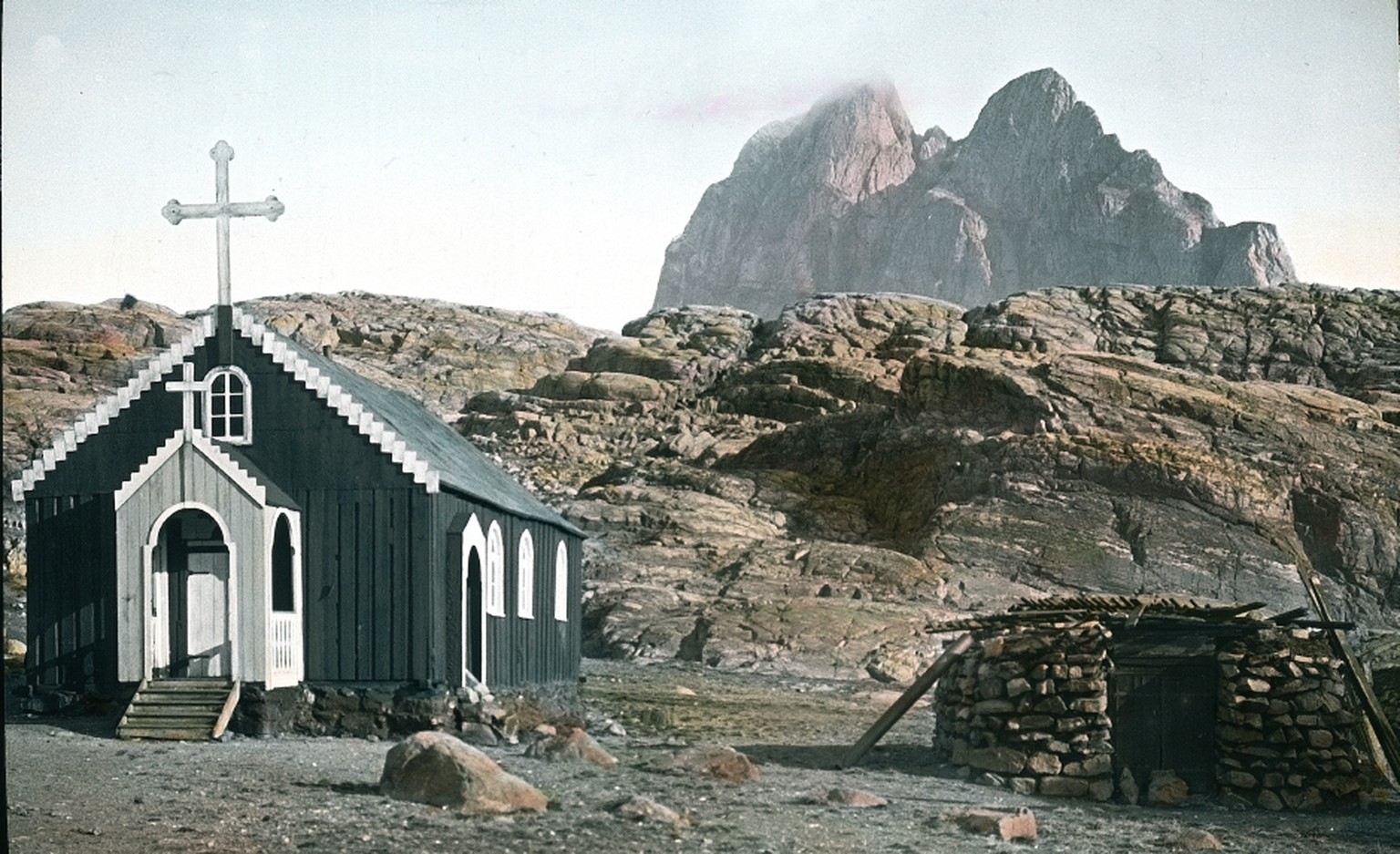 Die Kirche auf Uummannaq (zu Deutsch «der Robbenherz-Förmige», nach dem Berg im Hintergrund benannt), einer 12 km² grossen Insel in Südwestgrönland, wie sie auch in jedem anderen Dorf steht, 1909. <a target="_blank" href="https://de.wikipedia.org/wiki/Uummannaq#/media/File:Umanaq2.jpg">Heute sieht es dort so aus.</a>