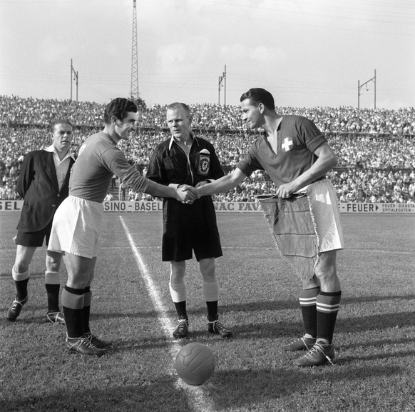 Der italienische Captain Pandolfini, links, und der Schweizer Roger Bocquet am 23. Juni 1954 beim freundschaftlichen Haendedruck und Wimpeltausch unter den Augen von Schiedsrichter Griffiths aus Wales ...