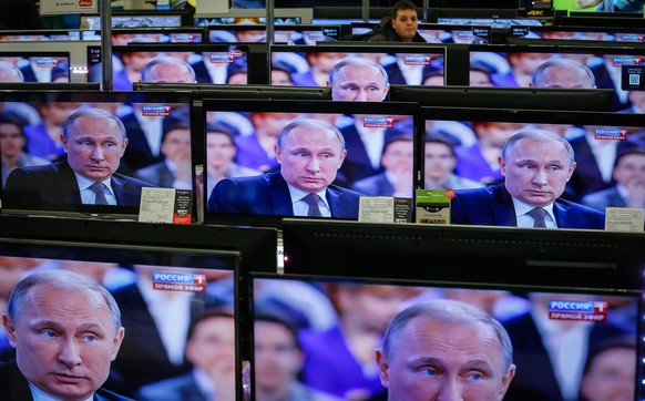 epaselect epa04707060 Russian man passes TV screens with Russian President Vladimir Putin an annual Q&amp;A (question-and-answer) nationwide live-broadcast TV and radio session in Moscow, Russia, 16 A ...