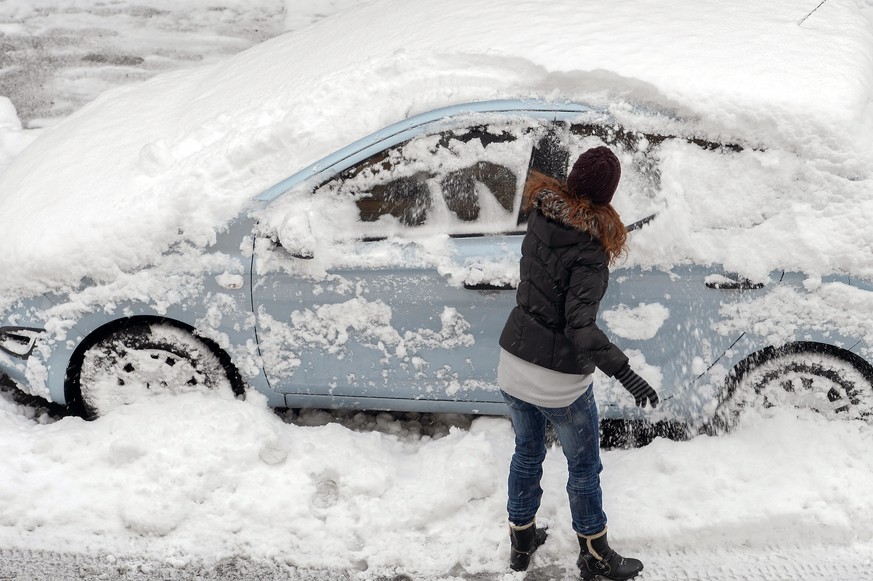 Eine Frau befreit ihr Auto vom Neuschnee in Zuerich am Sonntag, 28. Dezember 2014. Nach den gruenen Weihnachten kommt jetzt der Schnee auch bis ins Flachland. (KEYSTONE/Walter Bieri)
