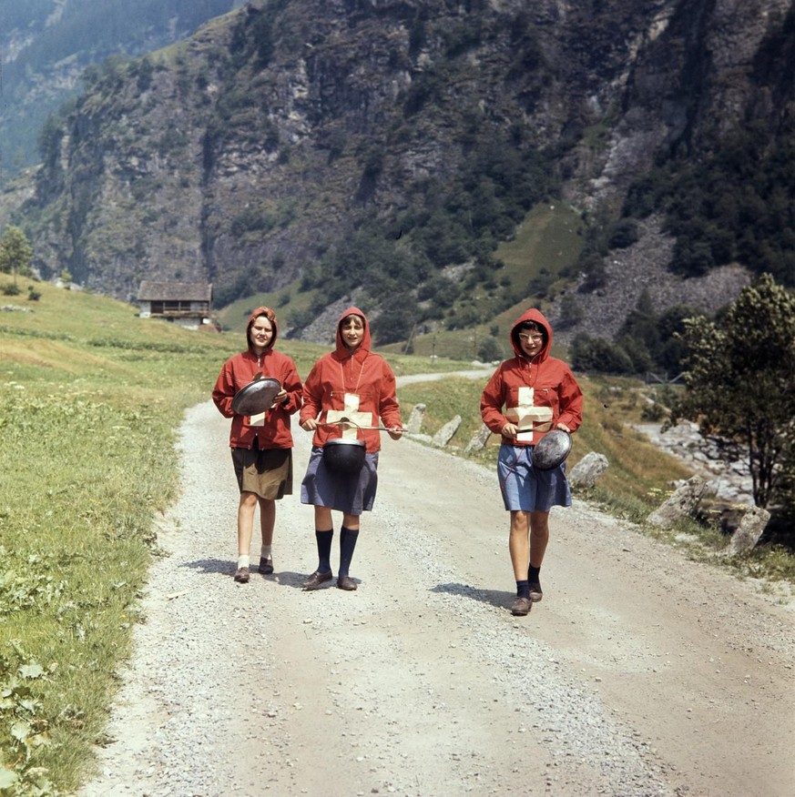 Pfadfinderinnen in Verkleidungen mit Schweizer Kreuz laden mit Schlaegen auf Pfannen zur Bundesfeier ein, aufgenommen am 1. August 1962 bei Arvigo im Calancatal, Kanton Graubuenden. (KEYSTONE/PHOTOPRE ...