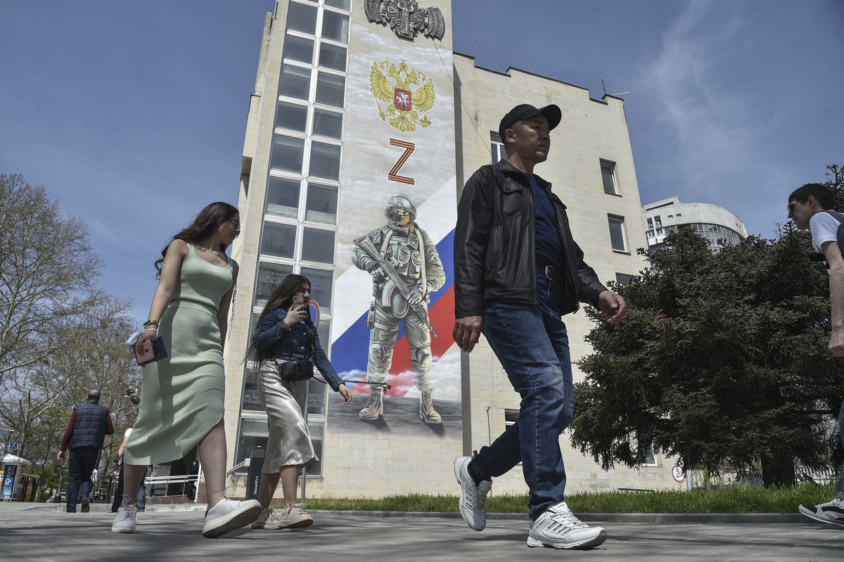 epa09910305 Pedestrians pass a mural depicting a Russian soldier, the Russian flag and double-headed eagle coat of arms as well as the 'Z' military symbol, on the side of a building in Simfe ...