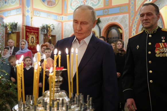 Russian President Vladimir Putin, center, accompanied by military personnel and their families, lights a candle while attending an Orthodox Christmas service at a church in Moscow Region, Russia, on W ...