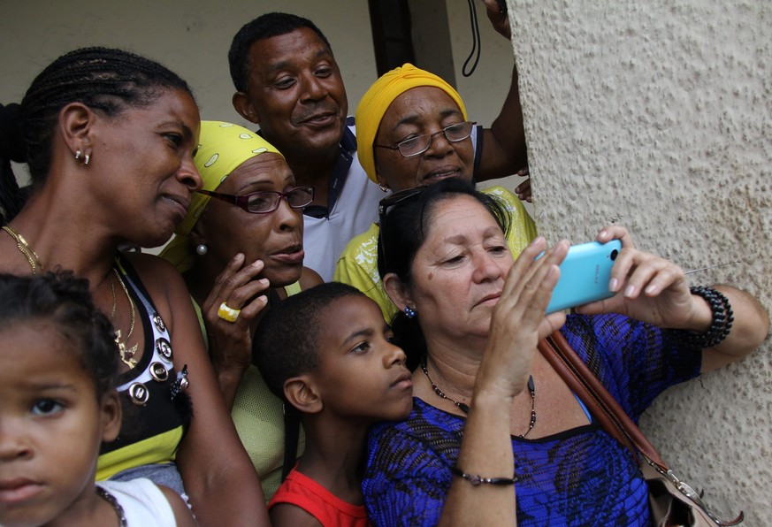 epa05223507 Cuban citizens look on a mobile phone at abroadcast of the US President Barack Obama&#039;s arrival at the Jose Marti Airport in Havana, Cuba, 20 March 2016. US President Barack Obama arri ...