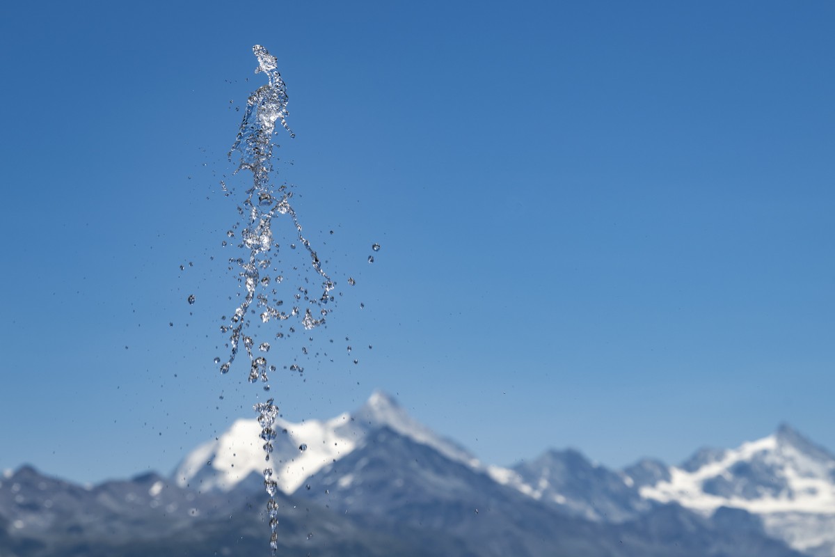 Le jet d'eau d'une fontaine est visible devant les montagnes valaisannes lors d'une chaude journee d'ete le jeudi 9 juillet 2026 depuis Crans-Montana. (KEYSTONE/Jean-Christophe Bot ...