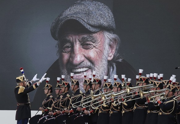 epa09618935 Members of the French Republican Guard music band play in front of a portrait of Jean-Paul Belmondo as they attend the tribute ceremony for the late French actor at the Hotel des Invalides ...