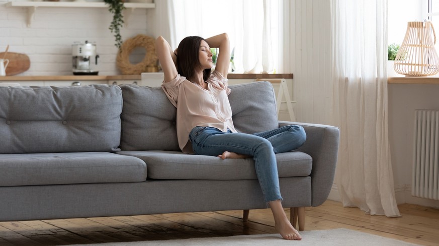 Serene lady housewife lounge sit on sofa feel fatigue napping hold hands behind head, calm young woman rest on comfort couch with eyes closed breath fresh air in cozy clean modern living room at home