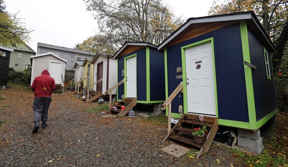 In this photo taken Thursday, Nov. 9, 2017, a resident walks past a row of tiny houses at a homeless encampment in Seattle where full size homes stand behind. Tiny homes could be the solution to all k ...