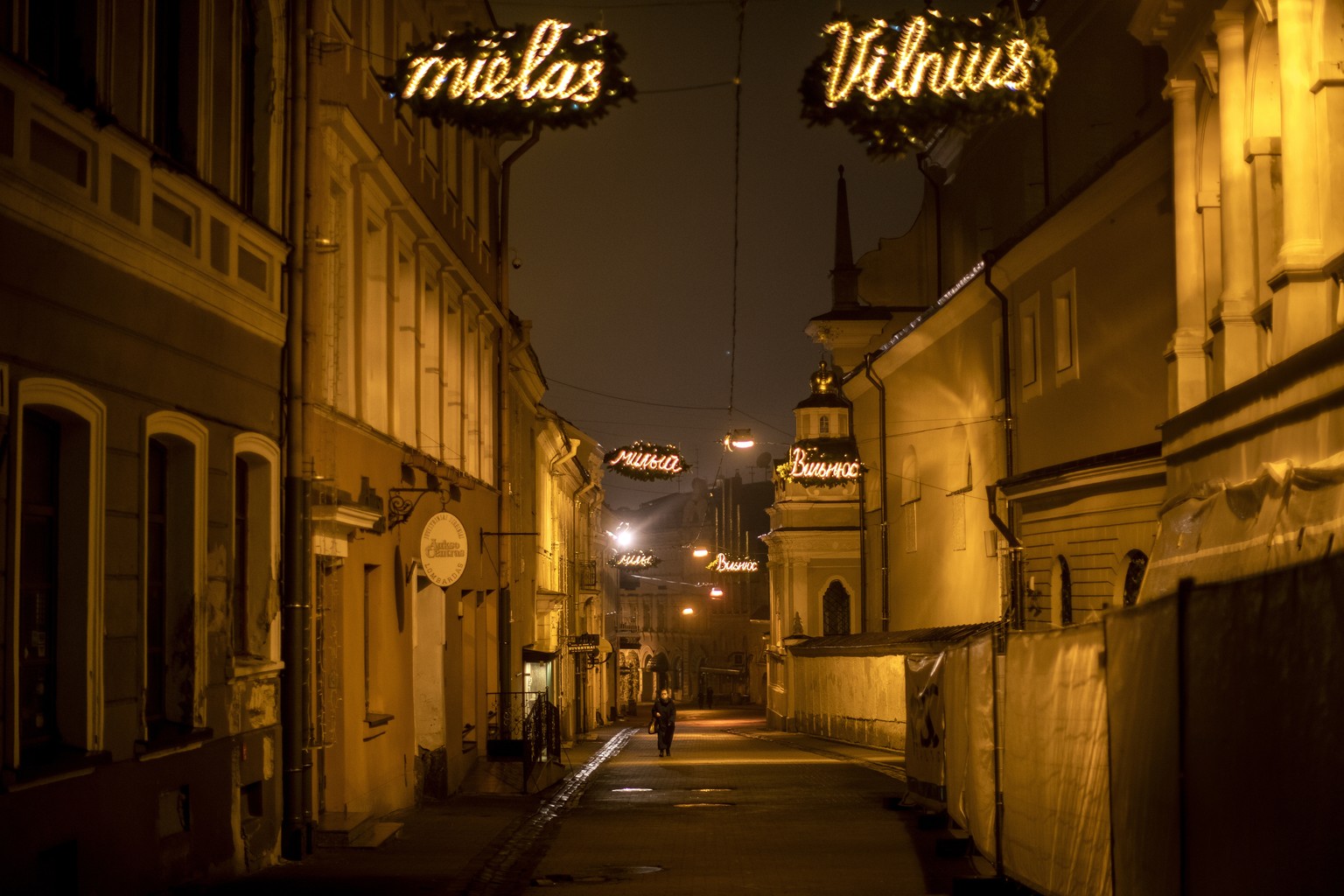 A woman wearing face mask to protect against coronavirus, walks on an empty street in Old Town in Vilnius, Lithuania, Thursday, Dec. 24, 2020. The catholic church cancelled all worship services but is ...