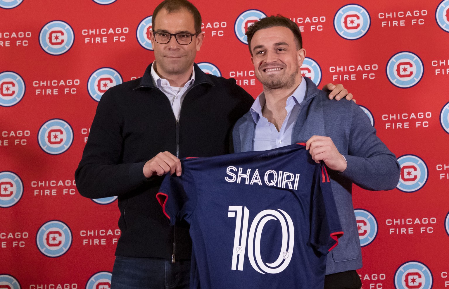 New Chicago Fire MLS soccer midfielder Xherdan Shaqiri smiles while posing with Chicago Fire sporting director Georg Heitz, left, in Chicago, Monday, Feb. 21, 2022. (Brian Cassella/Chicago Tribune via ...