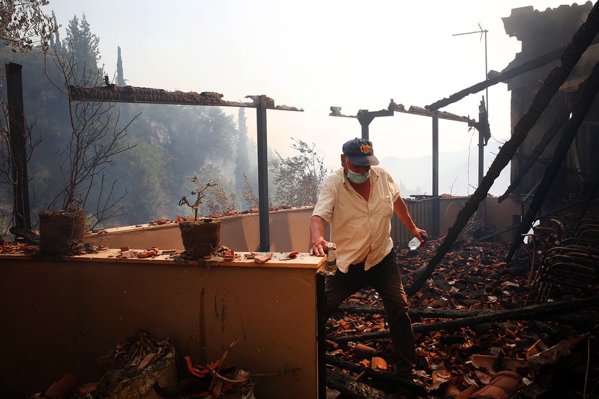 epa09398509 A man exits his burnt house in Viliza village in the area of Ancient Olympia, Peloponnese, Greece, 05 August 2021. Fires continued to rage in Olympia, in the Peloponnese, where more settle ...