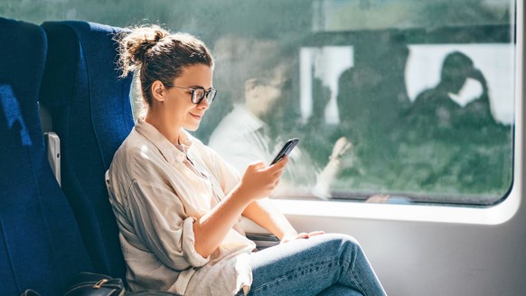 Young woman traveling by train and using phone.