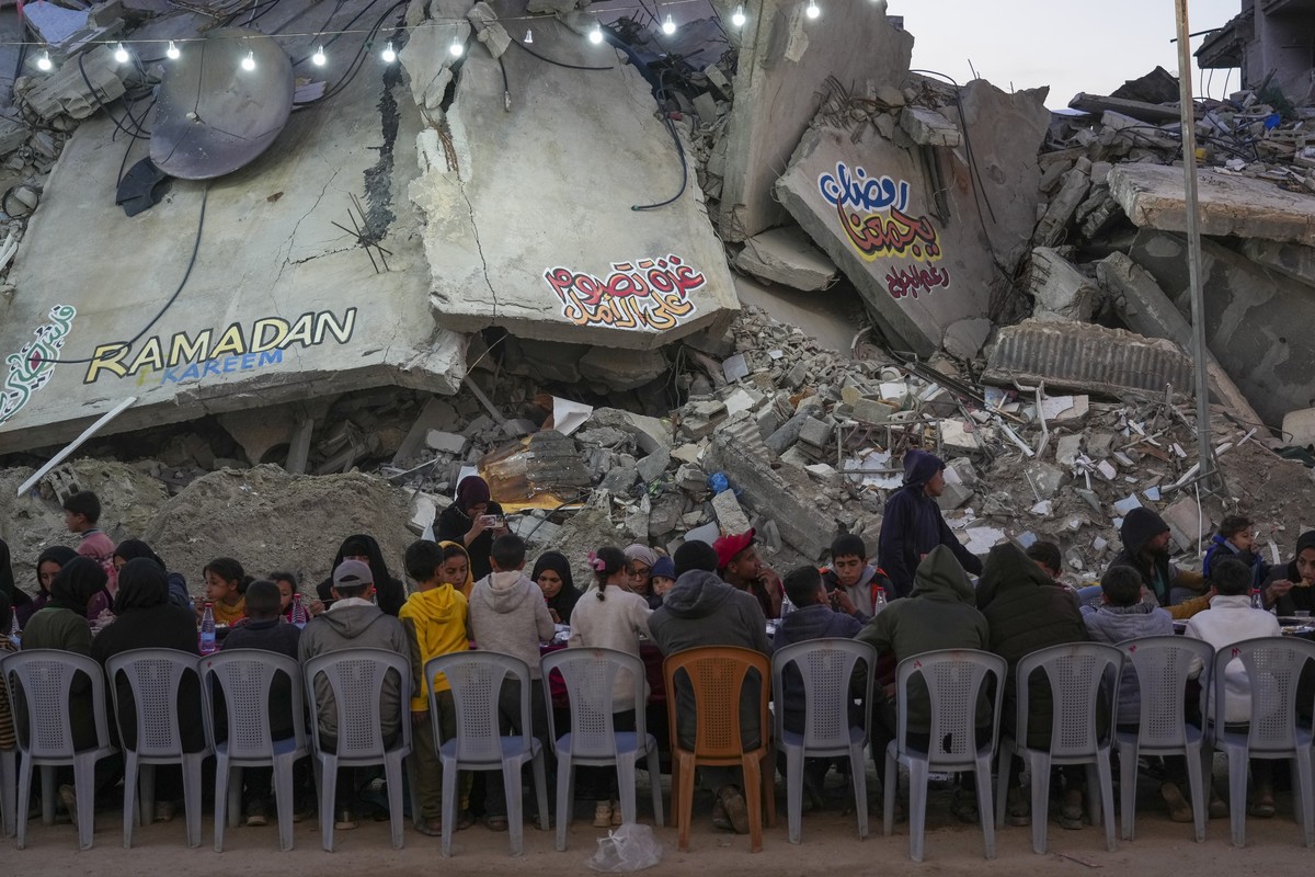 Palestinians sit at a large table surrounded by the rubble of destroyed homes and buildings as they gather for iftar, the fast-breaking meal, on the first day of Ramadan in Rafah, southern Gaza Strip, ...