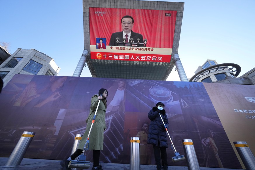 People walk past a large video screen at a shopping mall showing Chinese Premier Li Keqiang speaking during the opening session of the annual meeting of China&#039;s National People&#039;s Congress (N ...