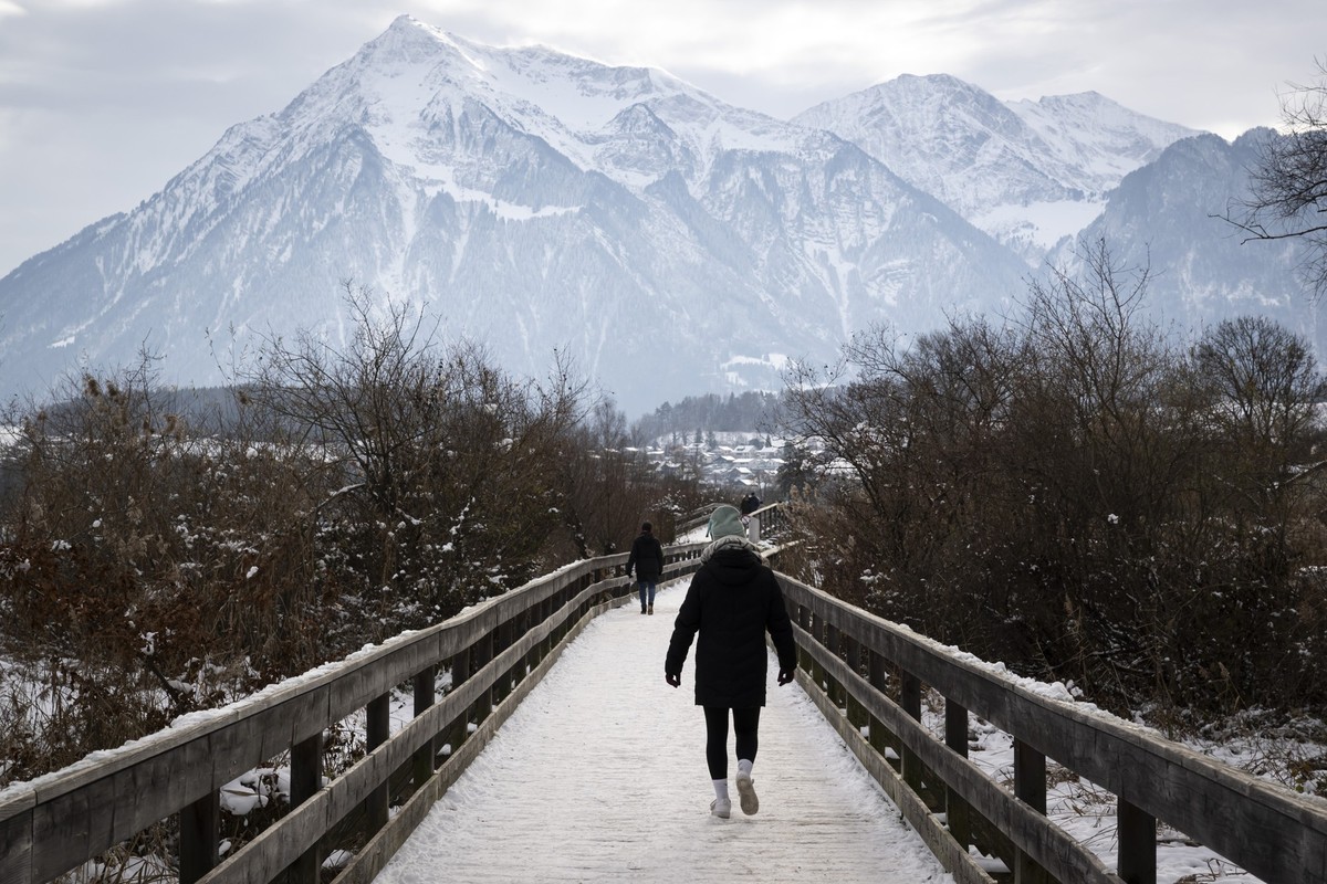 Mehrere Personen gehen ueber eine teilweise verschneite Bruecke am Ufer des Thunersees, im Hintergrund ragt der Gipfel des Niesen auf, am Sonntag, 23. November 2025 in Thun. Die Schweiz hat eine ausse ...