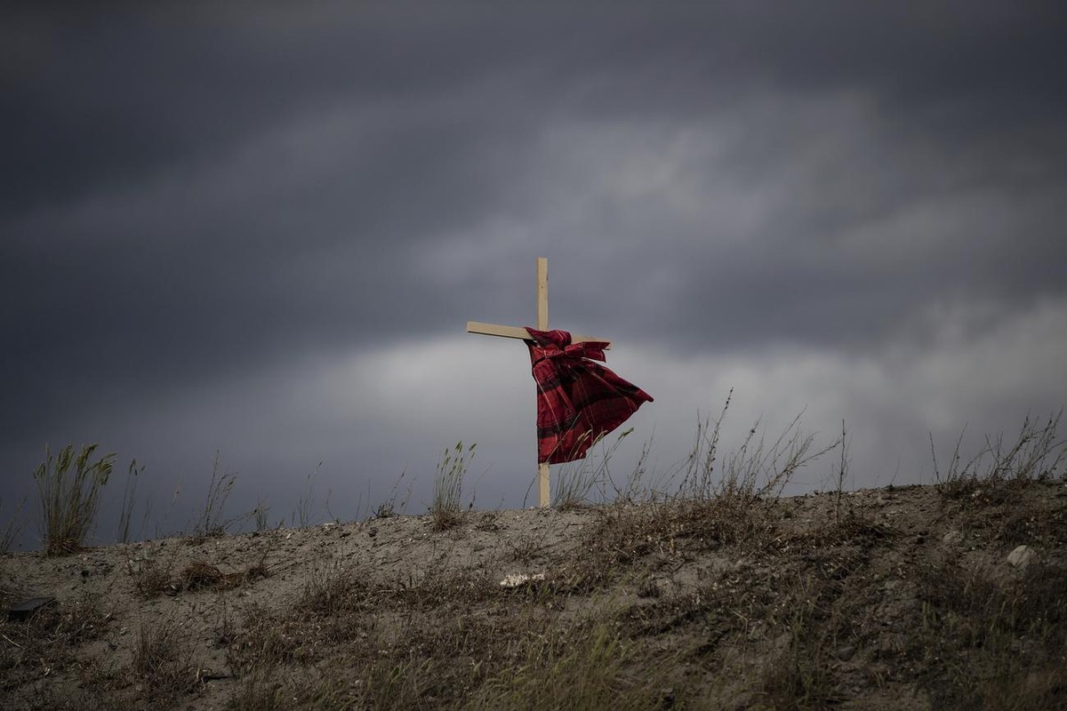 A child's dress hangs on a cross as it blows in the wind near the former Kamloops Indian Residential School, to honor the 215 children whose remains have been discovered buried near the facility  ...