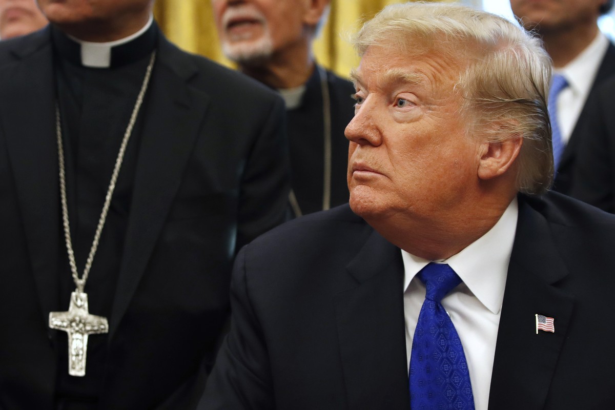President Donald Trump sits at the Resolute desk, surrounded by members of clergy, to sign H.R. 390, the "Iraq and Syria Genocide Relief and Accountability Act of 2018," in the Oval Office o ...