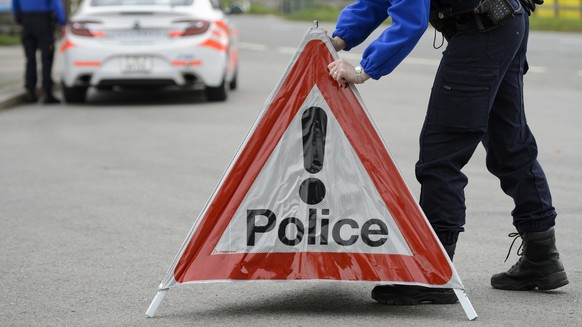 [Editor&#039;s note: photo mise-en-scene] A police officer from the cantonal police of Vaud installs a police warning triangle, in the foreground, while another officer stands next to a police car, in ...