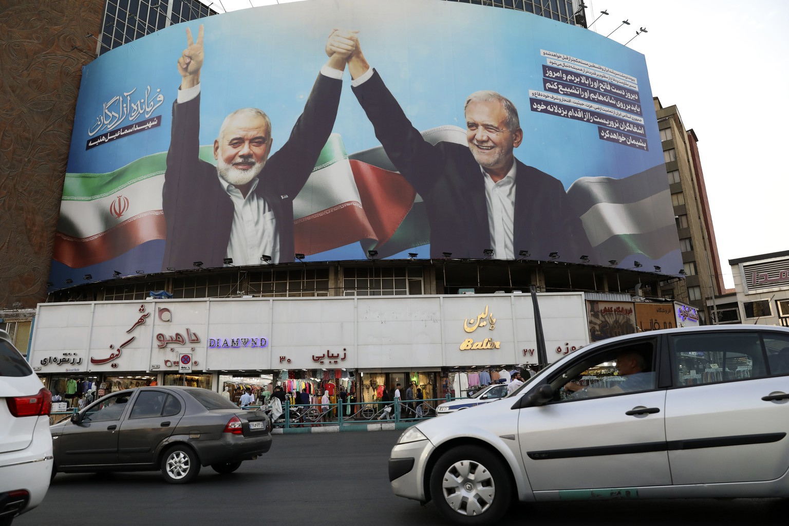 Vehicles drive past a huge banner showing the late Hamas leader Ismail Haniyeh, left, who was killed in an assassination last week, joining hands with Iranian President Masoud Pezeshkian, in a square  ...
