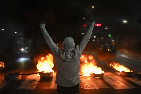 A protestor raises his arms in front of tires on fire in Caracas, Venezuela, Monday, July 29, 2024, the day after the presidential election. (AP Photo/Matias Delacroix)