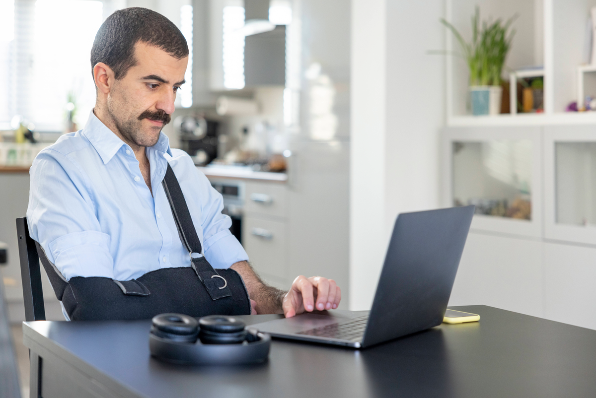 Man wearing arm sling working on laptop at home model released Symbolfoto property released WPEF04222