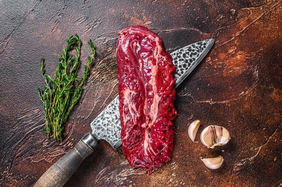 Raw Hanging Tender steak on a butcher knife . Dark background. Top view